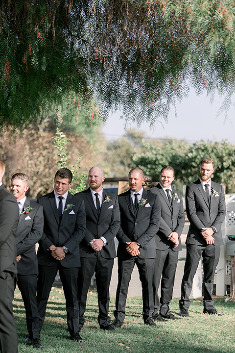  a lavender and black wedding in a garden – with the bride in a long sleeve lace gown and the groom in a black tuxedo – groomsmen in the ceremony 