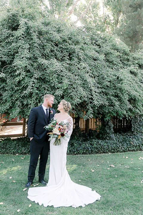  a lavender and black wedding in a garden – with the bride in a long sleeve lace gown and the groom in a black tuxedo – couple kissing 