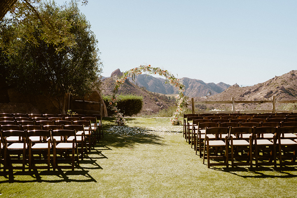  blush and beige wedding with a chic modern twist – the bride in a cap sleeved fitted gown and the groom in a black suit – ceremony arch