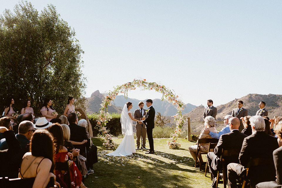  blush and beige wedding with a chic modern twist – the bride in a cap sleeved fitted gown and the groom in a black suit – vows at the ceremony