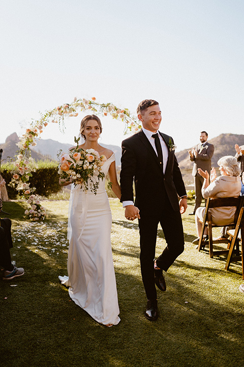  blush and beige wedding with a chic modern twist – the bride in a cap sleeved fitted gown and the groom in a black suit – walking down the altar 