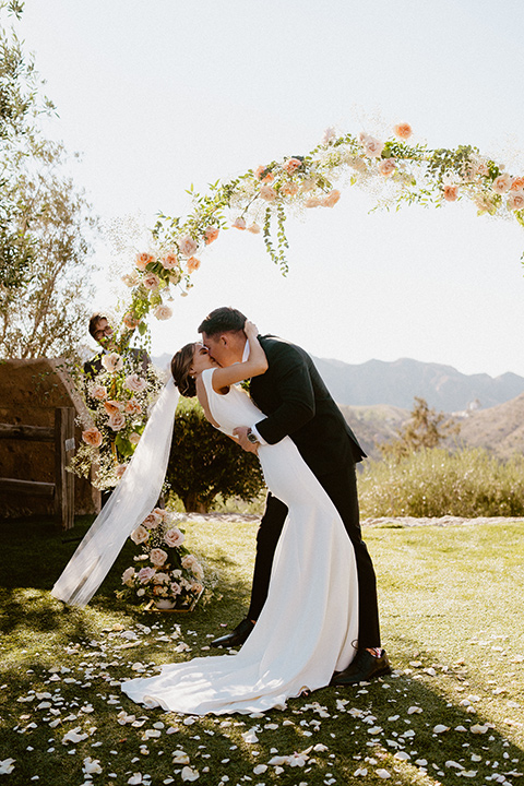  blush and beige wedding with a chic modern twist – the bride in a cap sleeved fitted gown and the groom in a black suit – first kiss 