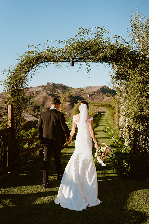  blush and beige wedding with a chic modern twist – the bride in a cap sleeved fitted gown and the groom in a black suit – couple walking 