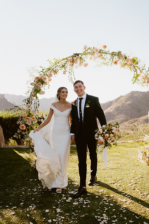  blush and beige wedding with a chic modern twist – the bride in a cap sleeved fitted gown and the groom in a black suit – couple walking