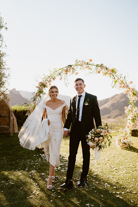  blush and beige wedding with a chic modern twist – the bride in a cap sleeved fitted gown and the groom in a black suit – couple walking 