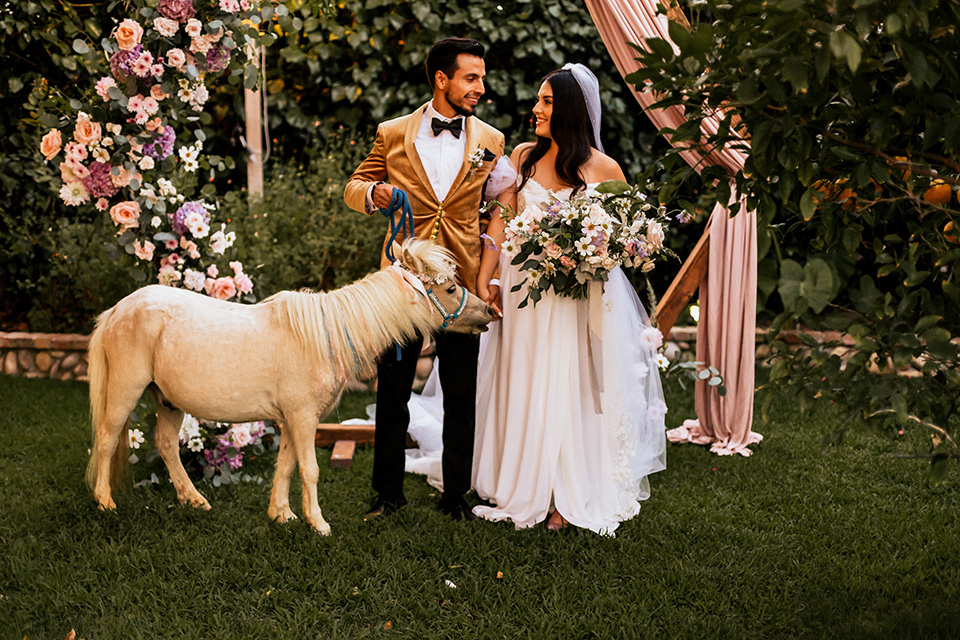  whimsical fairytale wedding with the groom in a gold velvet tuxedo – couple with mini pony