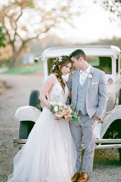  whimsical romance wedding with the bride in a ballgown and the groom in a light grey suit – couple by the car 