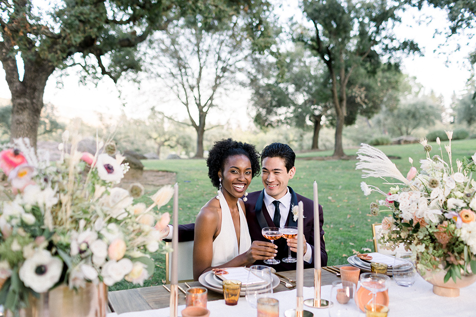  wine country wedding with the bride in a jumpsuit and the groom in a burgundy tux- couple at the table 