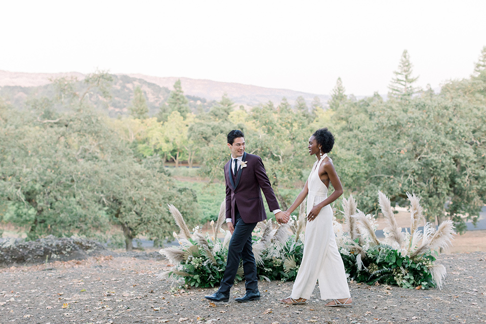  wine country wedding with the bride in a jumpsuit and the groom in a burgundy tux- walking 