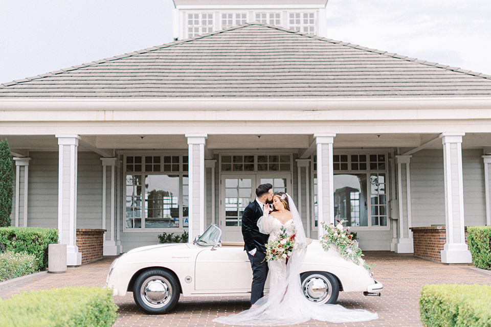  black and white modern wedding at the caramel mountain estate with the bride in a lace gown and the groom in a black velvet tuxedo – couple by the car 