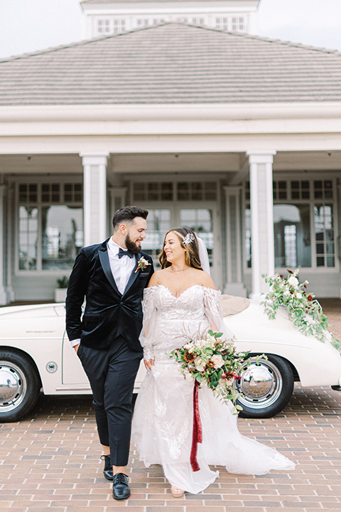  black and white modern wedding at the caramel mountain estate with the bride in a lace gown and the groom in a black velvet tuxedo –  couple walking by the car 