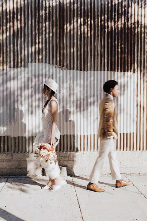  bohemian wedding with neutral colors and the groom in a gold velvet tuxedo – bride and groom walking outside venue 