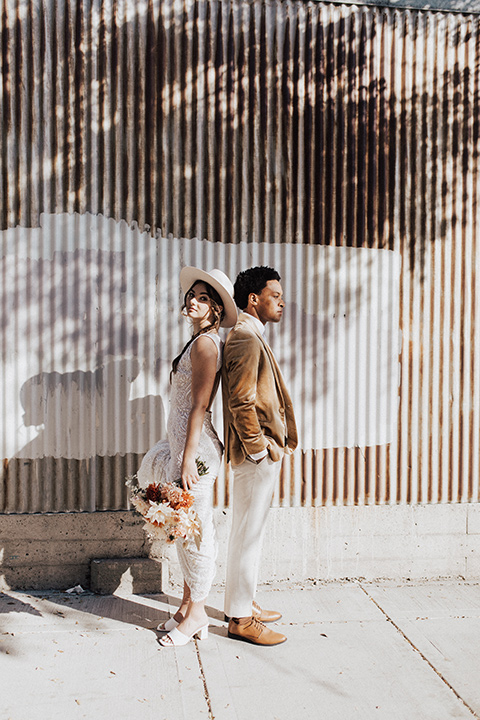  bohemian wedding with neutral colors and the groom in a gold velvet tuxedo – bride and groom walking outside venue 