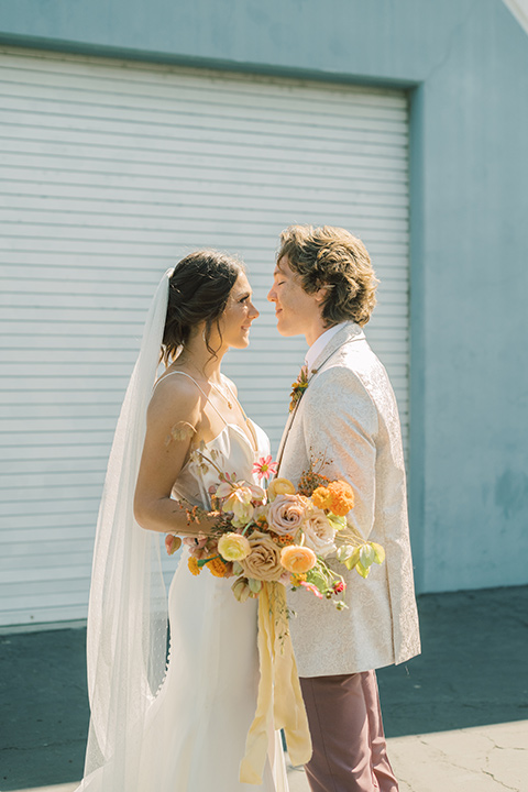  colorful modern wedding with the bride in a fitted gown and the groom in an ivory coat and pink pants – couple kissing outside