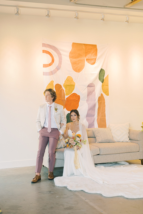  colorful modern wedding with the bride in a fitted gown and the groom in an ivory coat and pink pants – couple on the couch 