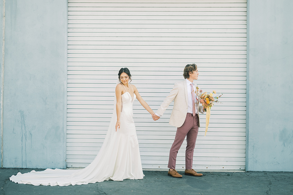  colorful modern wedding with the bride in a fitted gown and the groom in an ivory coat and pink pants – couple walking outside