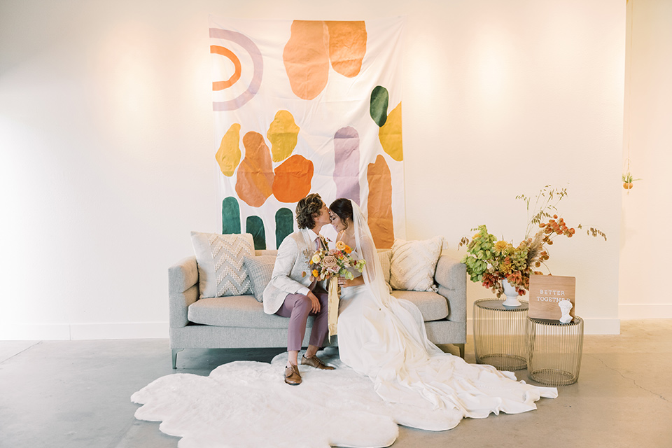  colorful modern wedding with the bride in a fitted gown and the groom in an ivory coat and pink pants – couple on the couch