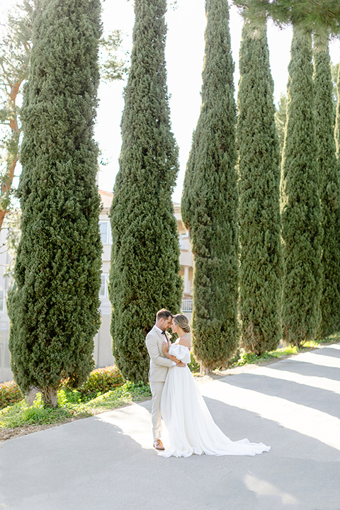  elevated cottagecore wedding design with the bride in a long sleeve ball gown and the groom in a tan suit - kissing by the hedges 