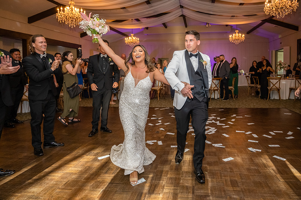  a modern black and white wedding with crystal details -the bride in a lace formfitting gown and the groom in a white + black tuxedo –entering the reception