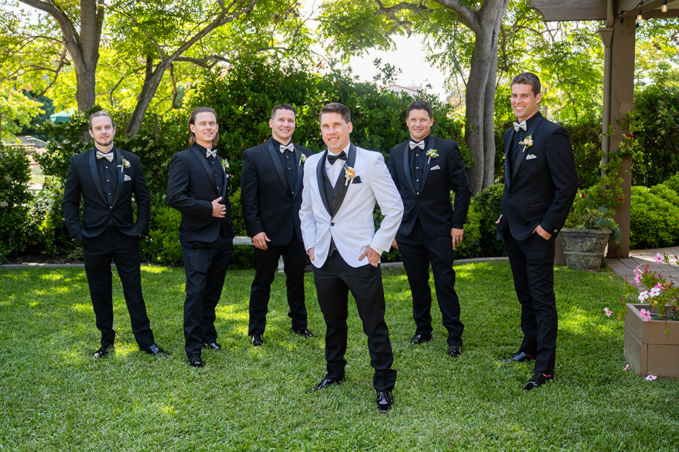  a modern black and white wedding with crystal details -the bride in a lace formfitting gown and the groom in a white + black tuxedo – groomsmen
