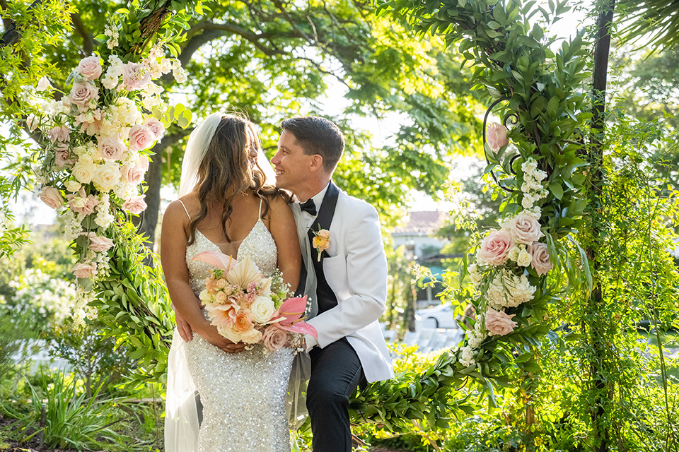  a modern black and white wedding with crystal details -the bride in a lace formfitting gown and the groom in a white + black tuxedo – couple in the greenery