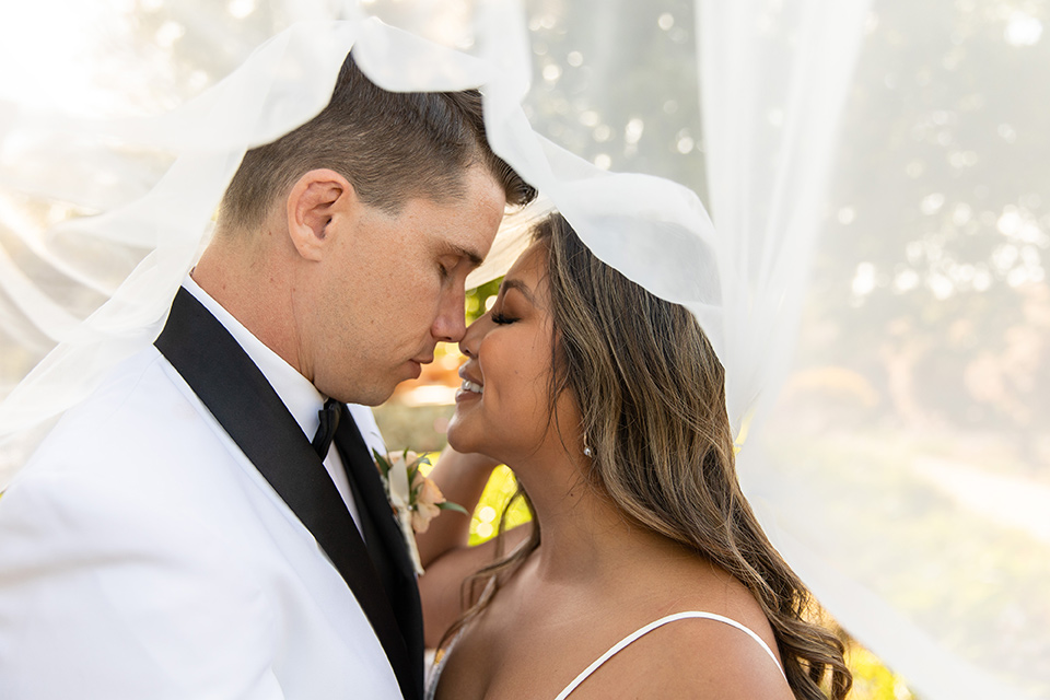  a modern black and white wedding with crystal details -the bride in a lace formfitting gown and the groom in a white + black tuxedo – under the veil