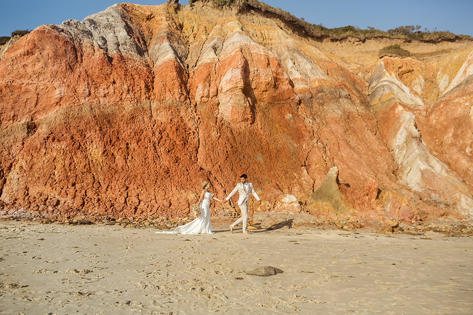  a neutral beachy elopement with the groom in a tan suit and the bride in a white lace dress – walking by the cliffs 