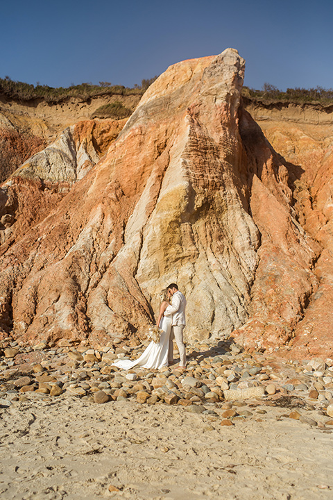  a neutral beachy elopement with the groom in a tan suit and the bride in a white lace dress – couple by the cliffs 