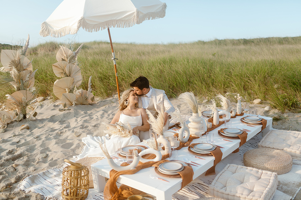  a neutral beachy elopement with the groom in a tan suit and the bride in a white lace dress – sitting at the picnic table 