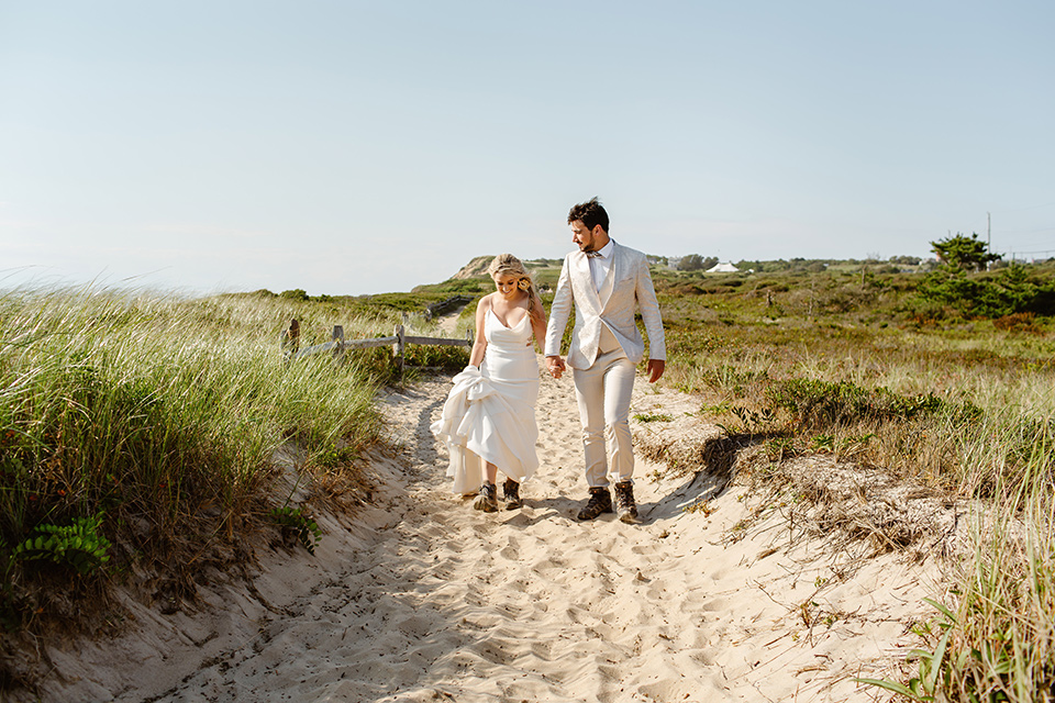  a neutral beachy elopement with the groom in a tan suit and the bride in a white lace dress – walking near the grasses 