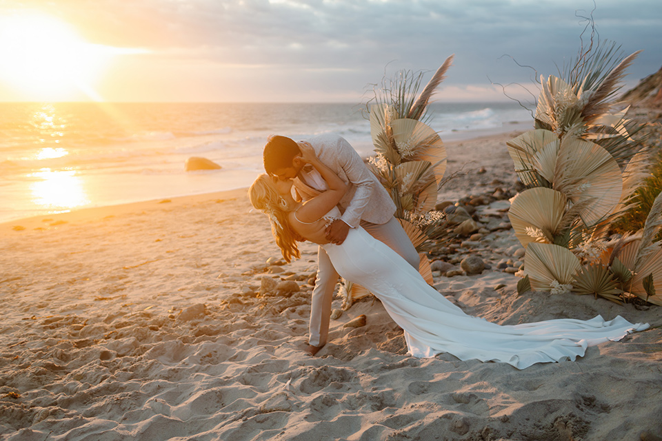  a neutral beachy elopement with the groom in a tan suit and the bride in a white lace dress – sunset kiss 