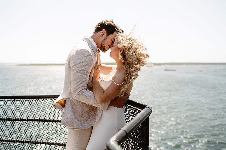  a neutral beachy elopement with the groom in a tan suit and the bride in a white lace dress – kissing by the water 