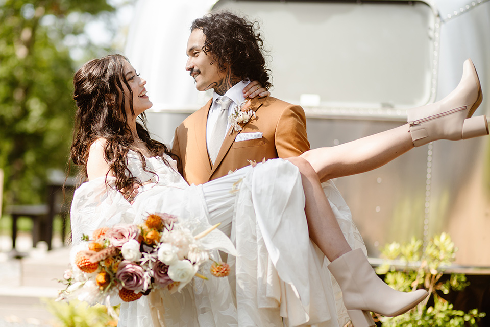  a boho caramel wedding inspo with an airstream and pampas grass – groom holding bride 