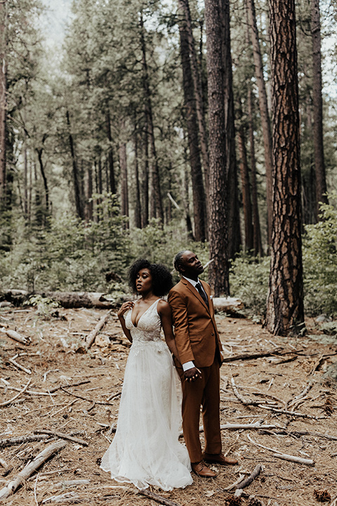  a woodland shoot in the sequoias with the groom in a caramel suit and the bride in a boho gown – couple standing back to back in the woods 