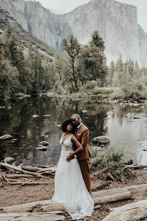  a woodland shoot in the sequoias with the groom in a caramel suit and the bride in a boho gown – couple on a log by the lake