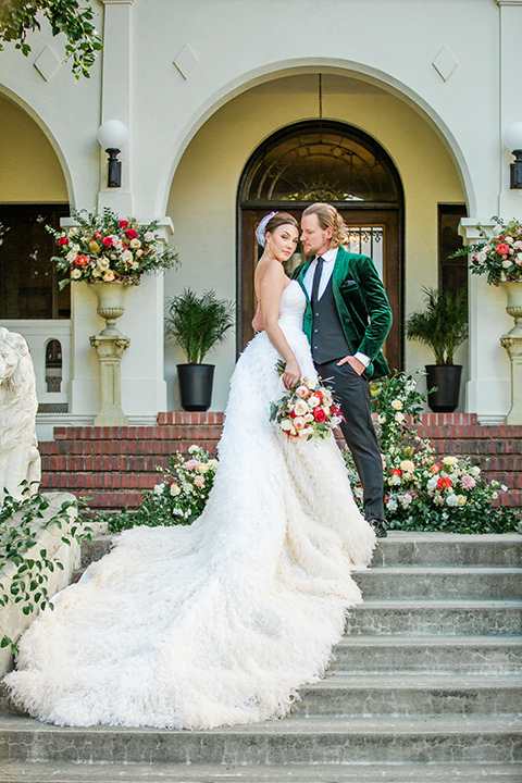  a dreamy whimsical wedding at a castle venue with the groom in a green velvet coat and the bride in a ballgown – couple on stairs 