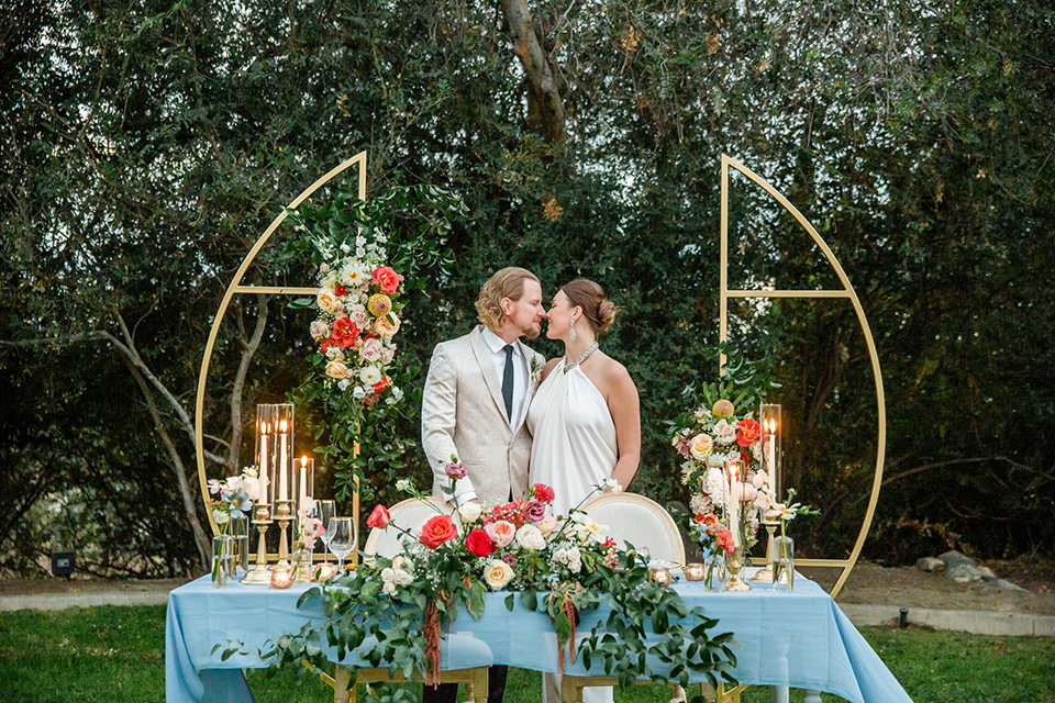  a dreamy whimsical wedding at a castle venue with the groom in a green velvet coat and the bride in a ballgown – couple by table 