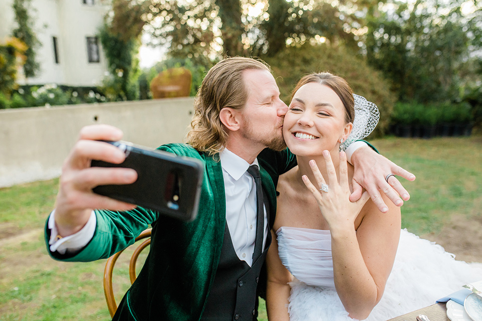  a dreamy whimsical wedding at a castle venue with the groom in a green velvet coat and the bride in a ballgown – couple taking a selfie 