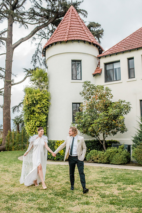  a dreamy whimsical wedding at a castle venue with the groom in a green velvet coat and the bride in a ballgown – couple walking on the grass 