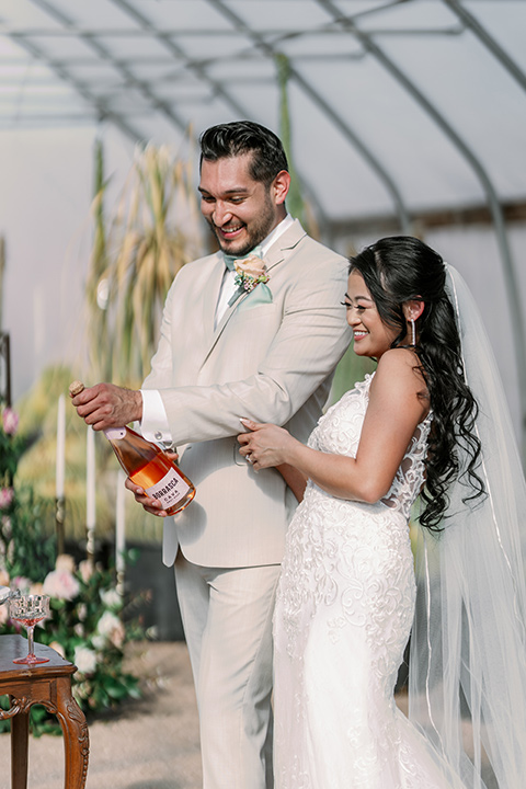  a garden romance wedding inspo with the bride in a luxe lace gown and the groom in a tan suit - drinking champagne 